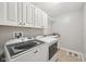 Clean laundry room featuring modern washer and dryer, upper cabinets, utility sink, and tiled floor at 3571 S Cedar Creek Ln, New Palestine, IN 46163