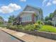 A two-story home with gray siding and a brick foundation is surrounded by lush greenery and garden beds at 4715 E New York St, Indianapolis, IN 46201