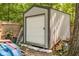 Exterior view of the metal shed with roll-up door, surrounded by tools, tree, and other backyard items at 3312 W 42Nd St, Indianapolis, IN 46228