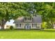 Charming tan farmhouse-style home with a covered front porch and lush green lawn and mature trees at 14855 E State Road 46, Columbus, IN 47203