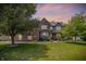 Charming two-story brick home with landscaped yard, mature trees, and warm inviting lighting at dusk at 1808 Woodfield Dr, Greenwood, IN 46143
