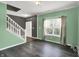 A cozy living room featuring mint walls, wood-look flooring, a large window, and an adjacent staircase, offering a comfortable living space at 12322 Cool Winds W Way, Fishers, IN 46037
