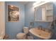 Powder room with blue walls, pedestal sink, toilet, mirror and complementary wall art at 9420 N Kenwood Ave, Indianapolis, IN 46260