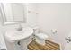 Elegant half-bath with a pedestal sink, modern fixtures, and a decorative mirror, complements the stylish wood flooring at 11320 Lynchburg Way, Indianapolis, IN 46229