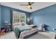 Cozy bedroom with blue walls, a ceiling fan, and a large window overlooking the trees at 705 Ridge Gate Dr, Brownsburg, IN 46112