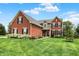 Charming red brick home featuring green grass, black shutters, and colorful flowers on the front porch at 13191 Roma, Carmel, IN 46074