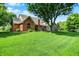 Backyard view showing lush grass, mature shade tree, brick home, and deck at 1411 N Claridge Way, Carmel, IN 46032