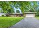 Single-story home featuring an attached garage, well-maintained lawn, mature landscaping, and a cracked asphalt driveway at 5205 Staughton Dr, Indianapolis, IN 46226