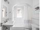 Bright bathroom features a pedestal sink, arched doorway, and a tub with a shower curtain at 5946 Guilford Ave, Indianapolis, IN 46220
