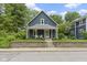 Blue two-story home showcasing a charming front porch, lush landscaping, and brick retaining wall at 6107 Broadway St, Indianapolis, IN 46220