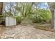 Spacious backyard patio with stone pavers, a white storage shed, and mature trees and bushes at 23 S Downey Ave, Indianapolis, IN 46219