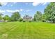 Home featuring a large front lawn, mature trees, and a gravel driveway under a sunny, partly cloudy sky at 1130 E 105Th St, Carmel, IN 46280