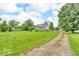 Home with a large front lawn, mature trees, and a gravel driveway set against a blue sky at 1130 E 105Th St, Carmel, IN 46280