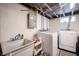 Basement laundry area with modern washer, dryer, utility sink and visible pipes and unfinished ceiling at 4927 Caroline Ave, Indianapolis, IN 46205