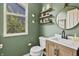 Stylish powder room with wood vanity, white sink, round mirror, floating wood shelves, and green walls at 5917 Bartley Dr, Noblesville, IN 46062
