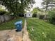 A spacious backyard featuring a detached garage with overgrown grass, a trash bin, and a cement path at 1226 Hiatt St, Indianapolis, IN 46221