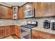 Close up of the kitchen featuring stainless steel stove, microwave, coffee maker, stone backsplash, and brown wood cabinets at 15410 Mission Hills Dr, Carmel, IN 46033