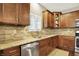 Kitchen area features granite countertops, stainless steel appliances, natural stone backsplash, and brown wood cabinets at 15410 Mission Hills Dr, Carmel, IN 46033
