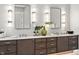 Close-up of a bathroom vanity with modern lighting fixtures, dual sinks, stylish mirrors and brown cabinetry at 6115 Stonegate Run, Zionsville, IN 46077