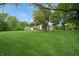 Expansive front lawn with mature trees surrounding a cream-colored single story home under a sunny sky at 6115 Stonegate Run, Zionsville, IN 46077