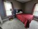 Cozy bedroom featuring a bed with a red comforter, side table with lamp, and windows with sheer curtains at 2824 Brown St, Anderson, IN 46016