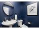Chic half bathroom features a dark blue wall, round mirror, and white sink and toilet at 10262 Rieslaner Cir, Zionsville, IN 46077