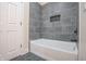 Modern bathroom featuring gray tiled walls, a built-in niche, and a sleek white bathtub at 5511 E University Ave, Indianapolis, IN 46219