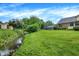 Expansive green backyard with flowing creek and mature trees surrounding brick and yellow siding home at 4070 Serenity Way Ct, Greenwood, IN 46142