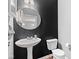 Elegant half-bathroom with a pedestal sink, stylish round mirror, and modern fixtures on a dark accent wall at 9046 Sparta Dr, Fishers, IN 46038