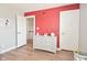 Cozy bedroom featuring light wood floors, red accent wall, and white dresser with baby monitor at 2734 Chalbury Dr, Plainfield, IN 46168