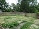 A fenced backyard features a garden and grass and a view of a storage shed and lush trees at 3518 Woodale Rd, Indianapolis, IN 46234