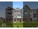 A row of three-story townhouses with varied architectural styles and brick and siding exteriors sit on a well-manicured lawn at 6038 Windsor Dr, McCordsville, IN 46055