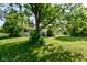 Lush backyard with a large tree providing shade and a view of the home's rear exterior at 10065 E 25Th St, Indianapolis, IN 46229