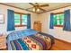 Bright bedroom featuring a ceiling fan, hardwood trim, and windows with blue curtains and a colorful patterned blanket at 2808 Woodside Dr, Plainfield, IN 46168
