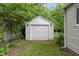 Exterior view of a detached garage with a white door surrounded by lush greenery at 4517 E 16Th St, Indianapolis, IN 46201