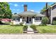 Charming bungalow featuring a landscaped yard, brick chimney, and inviting front porch with flowers at 4721 Carrollton Ave, Indianapolis, IN 46205