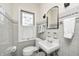 A charming bathroom has a sink, toilet, decorative mirror and sconce and a bright window at 5430 N Kenwood Ave, Indianapolis, IN 46208