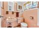 Vintage bathroom with pink tile, toilet, sink, vanity, medicine cabinet, and window at 1340 Eustis Dr, Indianapolis, IN 46229