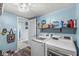 Light blue laundry room featuring modern washer, dryer, storage shelf, and wood-look flooring at 5299 Breakers Way, Carmel, IN 46033