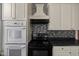 Kitchen with mosaic backsplash, stove, and oven plus white cabinets and overhead exhaust and cooktop at 761 N Holmes Ave, Indianapolis, IN 46222