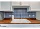 A well-lit kitchen sink and faucet with a blue patterned backsplash and wooden countertops at 8540 E 37Th Pl, Indianapolis, IN 46226