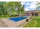 An inground blue pool is surrounded by greenery and sits behind a brick house at 10174 N County Road 471 E, Pittsboro, IN 46167