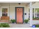Close up of charming porch with a porch swing, house number, and coral front door with plants at 6142 Evanston Ave, Indianapolis, IN 46220