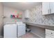 Functional laundry room with a washer, dryer, workspace, storage cabinets, and patterned wallpaper at 6664 Kara Ln, Brownsburg, IN 46112