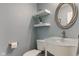 Powder room with blue walls, floating shelves, an oval mirror above the sink, and a white toilet and sink at 9593 W Constellation Dr, Pendleton, IN 46064