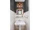 Stylish half-bathroom featuring a pedestal sink, dark accent wall, and decorative mirror at 4455 Broadway St, Indianapolis, IN 46205
