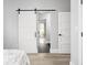 Light-filled bedroom featuring a sliding barn door, hardwood floors, and decorative patterned curtains at 5678 N College Ave, Indianapolis, IN 46220