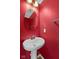 Small bathroom features a stylish oval mirror and a classic pedestal sink against vibrant red walls at 3230 Hemlock St, Whiteland, IN 46184