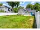 Large backyard with lush grass, a tree stump, a fire pit, and a white fence surrounding the property at 206 Olive St, Arcadia, IN 46030