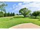Large backyard featuring lush green grass, mature trees, a fire pit, and a glimpse of the neighborhood pond at 10548 Magenta Dr, Noblesville, IN 46060